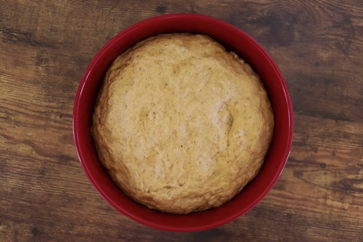 Orange dough in a red bowl sitting on a wooden surface.