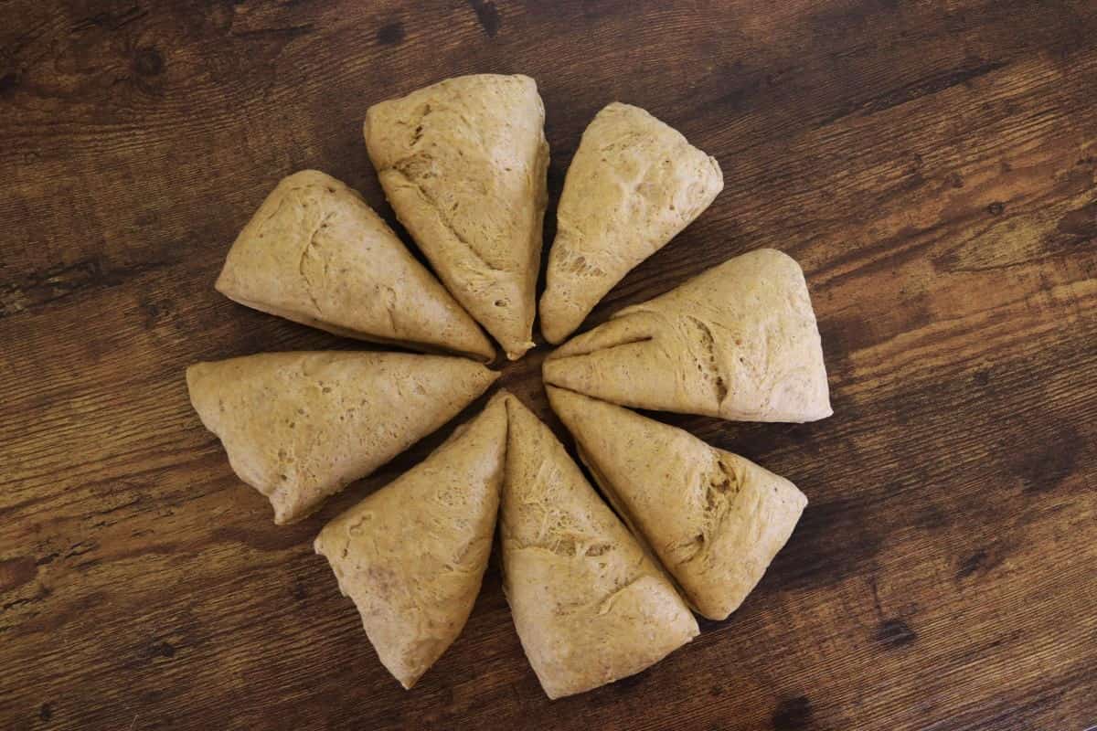 Circle of pie shaped dough pieces sitting on a wooden surface.
