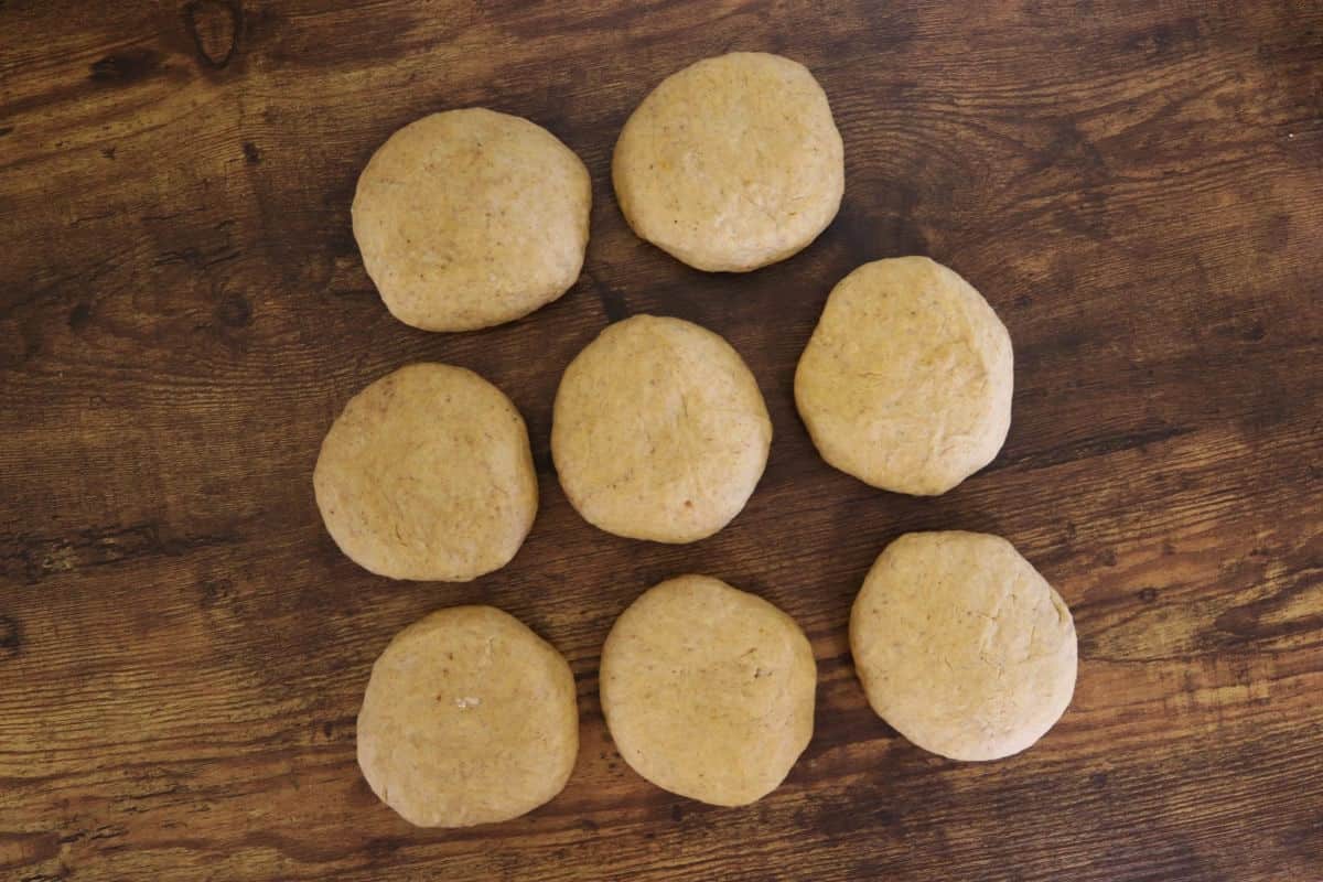 Eight balls of orange colored dough sitting on a wooden surface.