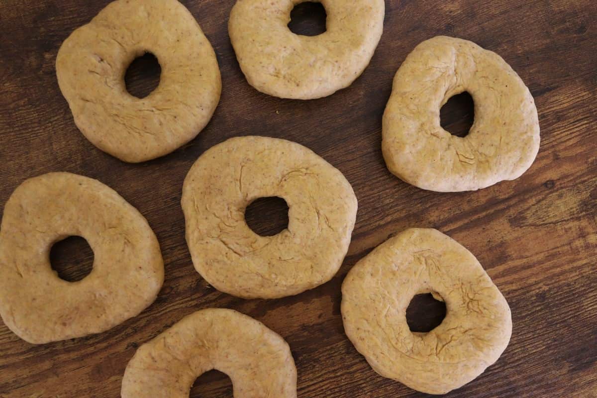 Raw, orange colored bagels sitting on a wooden surface.