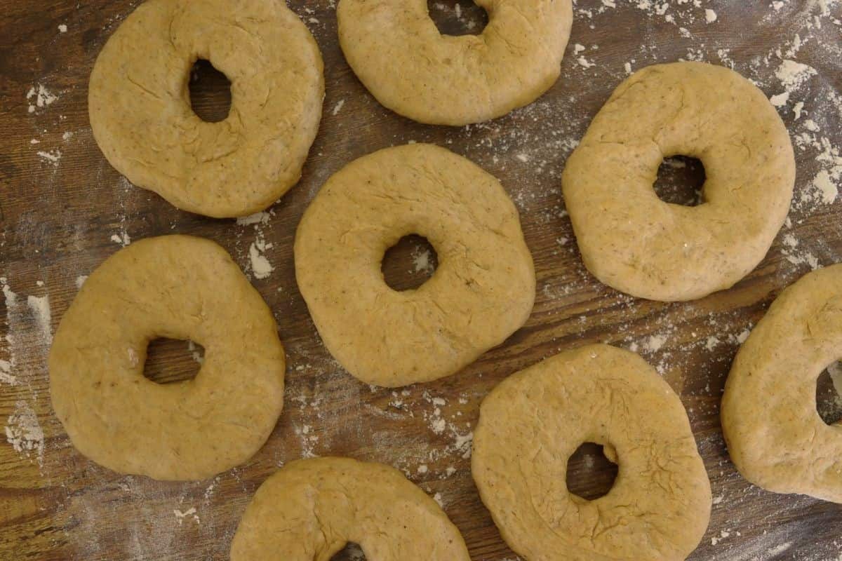 Raw, orange colored bagels sitting on a floured wooden surface.