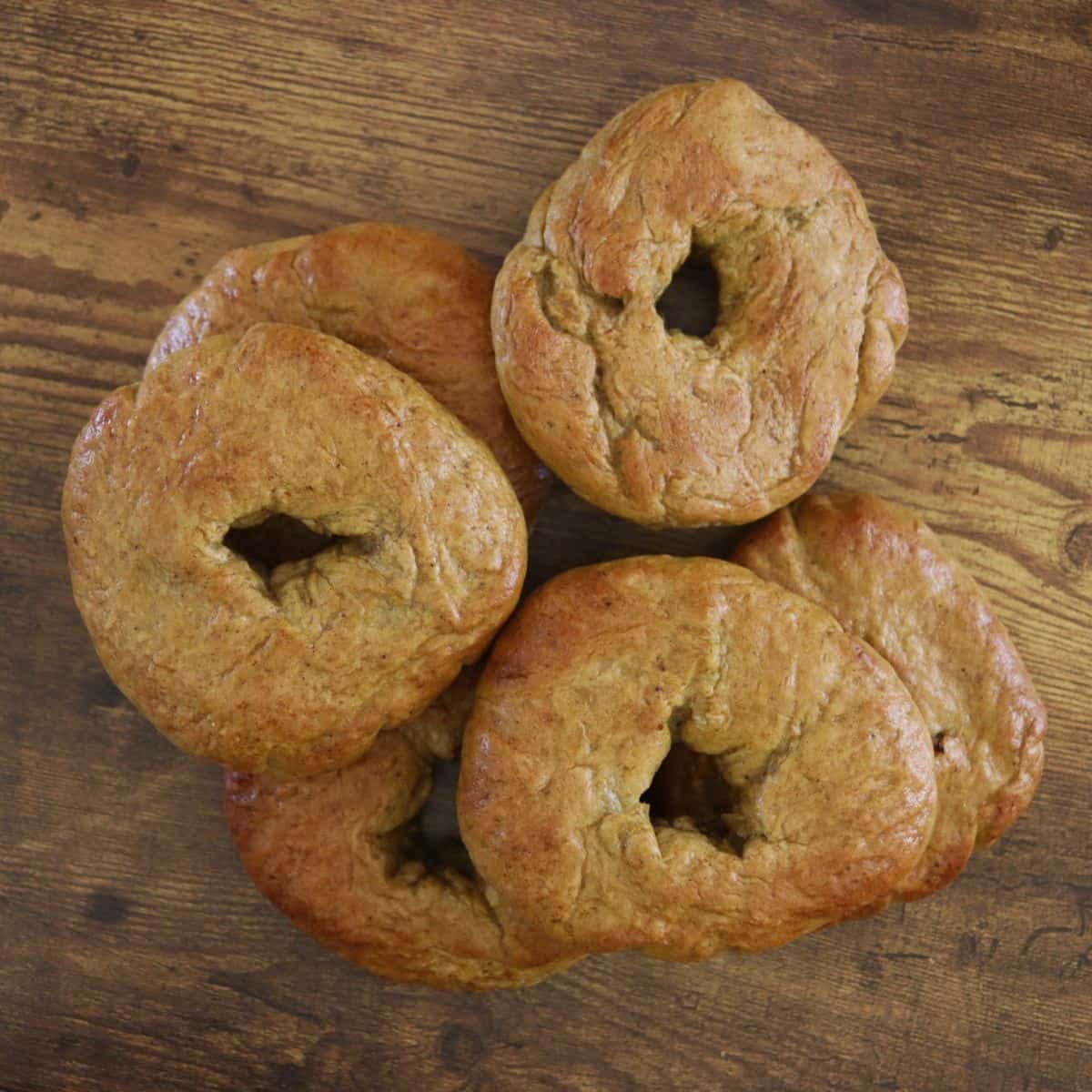 Orange colored bagels sitting in a pile on a wooden surface.
