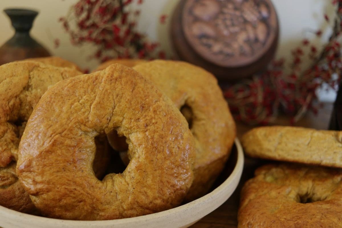 A bowl of bagels, with other bagels on the table next to it.