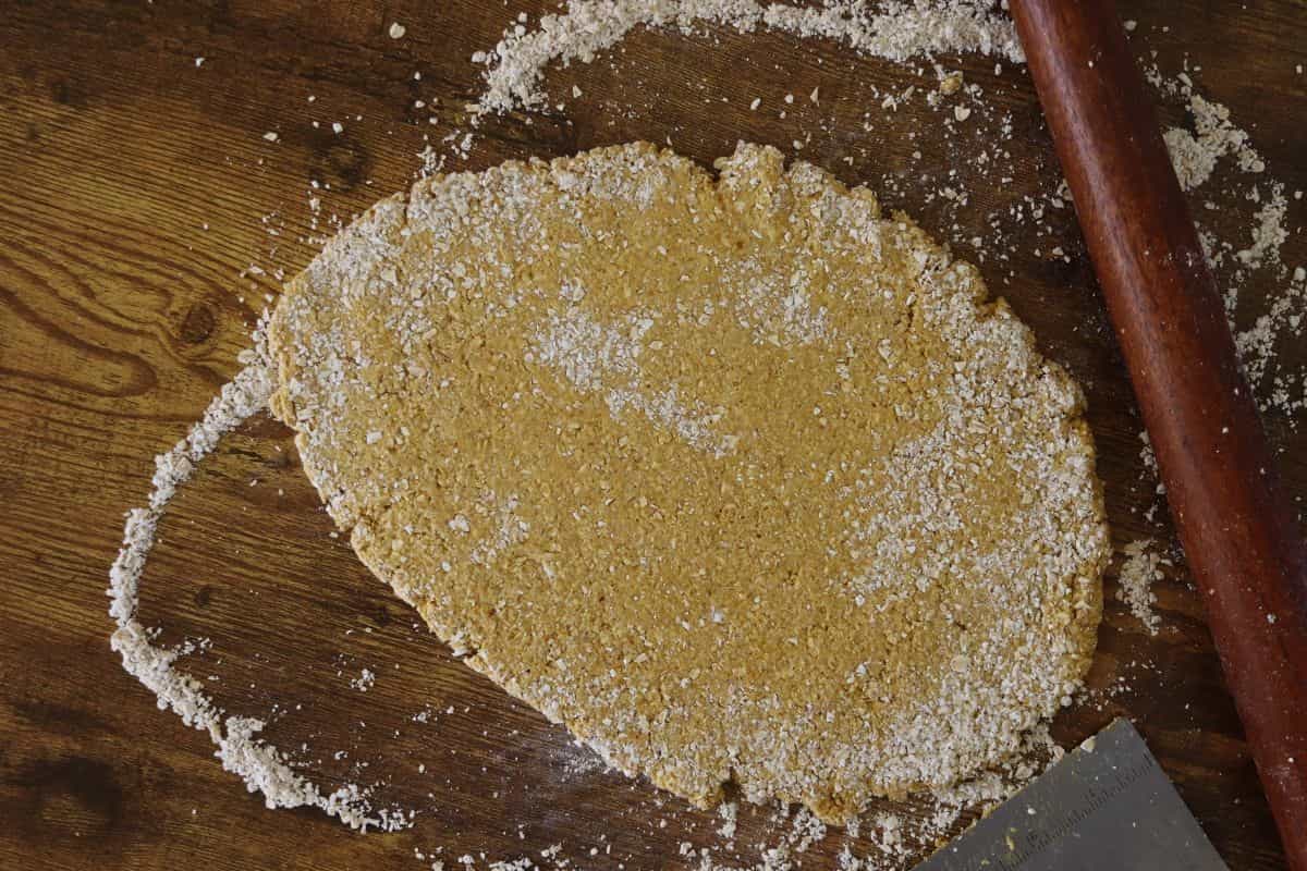 Orange, grainy dough rolled out on a floured wooden surface.