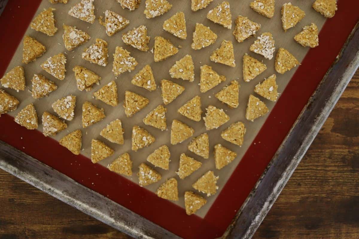 Small triangular shaped dough pieces on a silicone lined baking sheet.