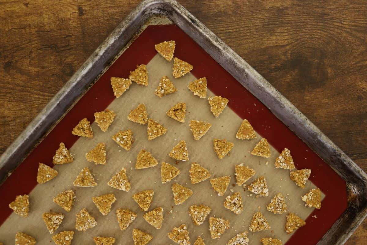 Baked, triangular shaped cat treats on a silicone lined baking sheet.