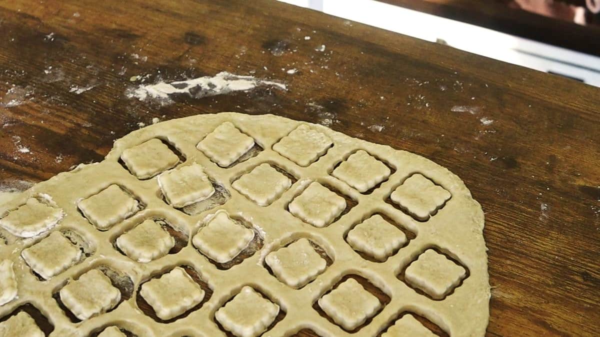 Dough rolled out on a wooden surface with square shapes cut into it.