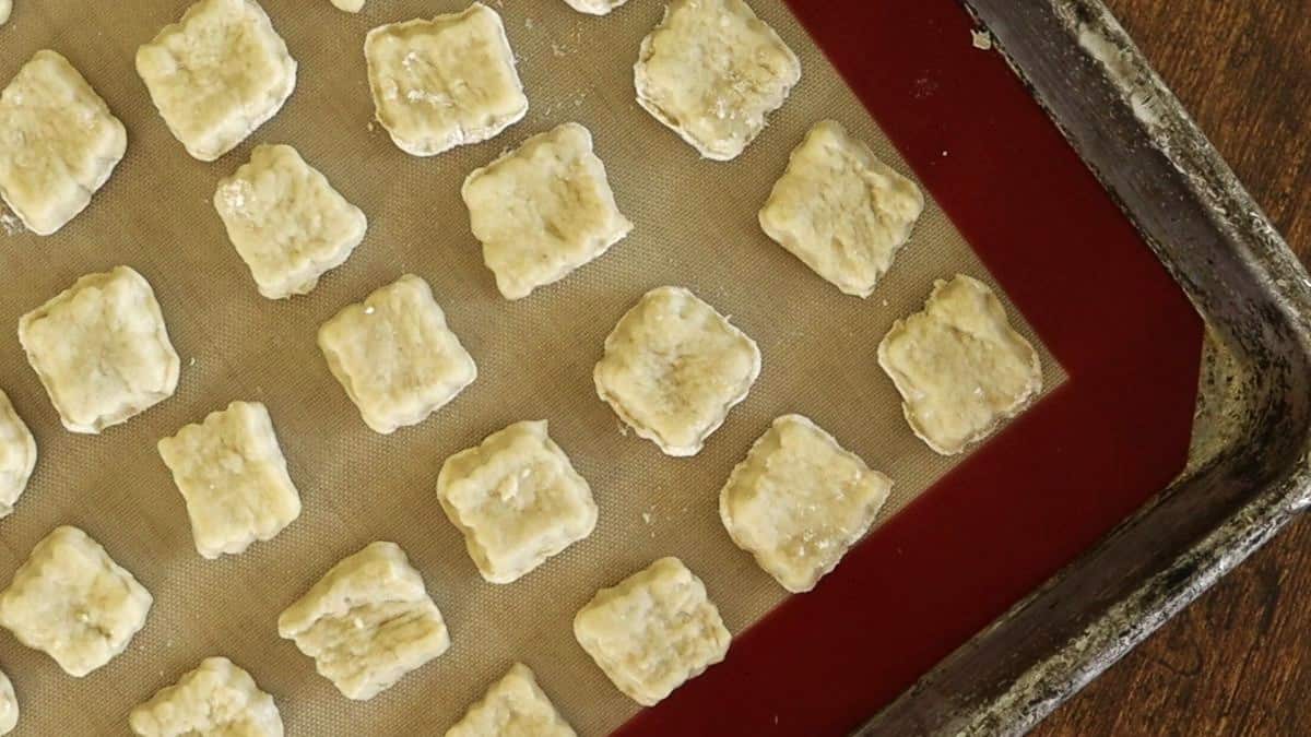 Square raw crackers sitting on a silicone lined sheet.