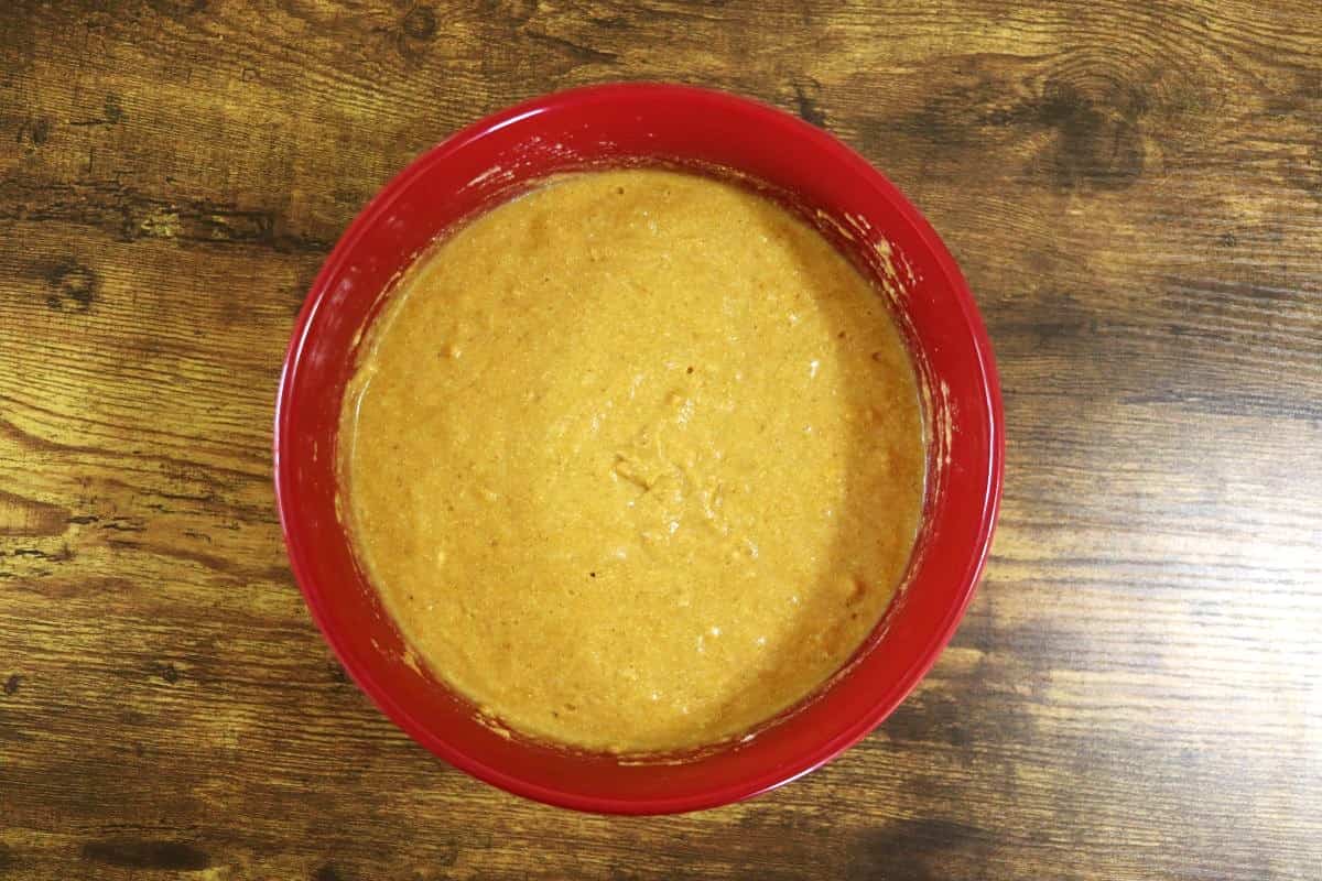 Orange colored batter in a red bowl sitting on a wooden surface.