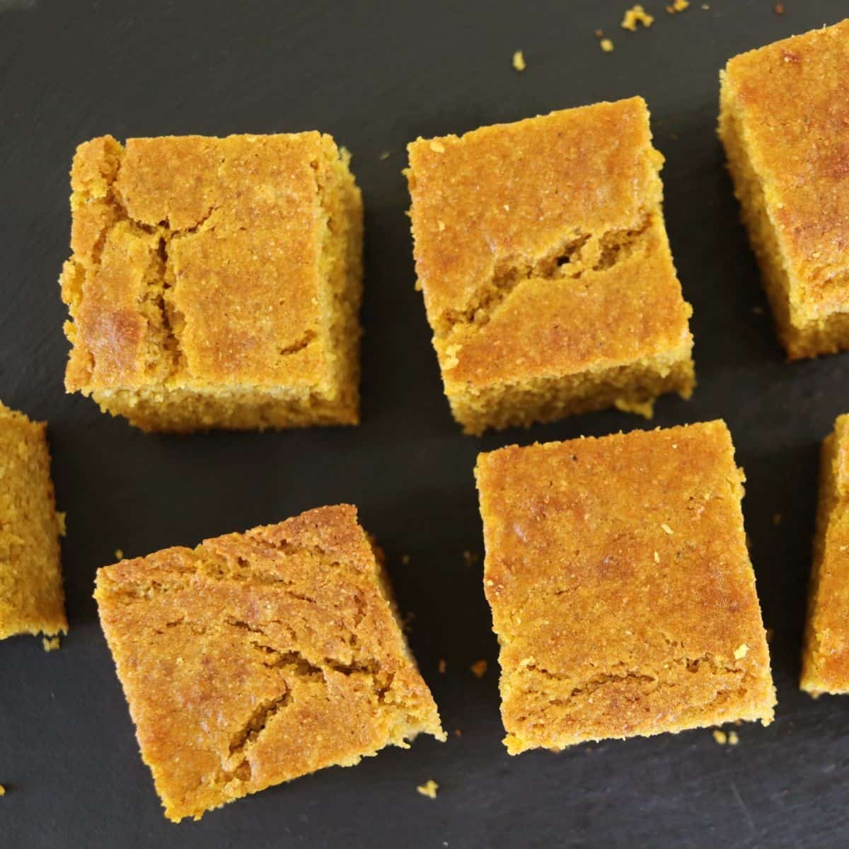 Square pieces of orange quick bread sitting on a black surface.