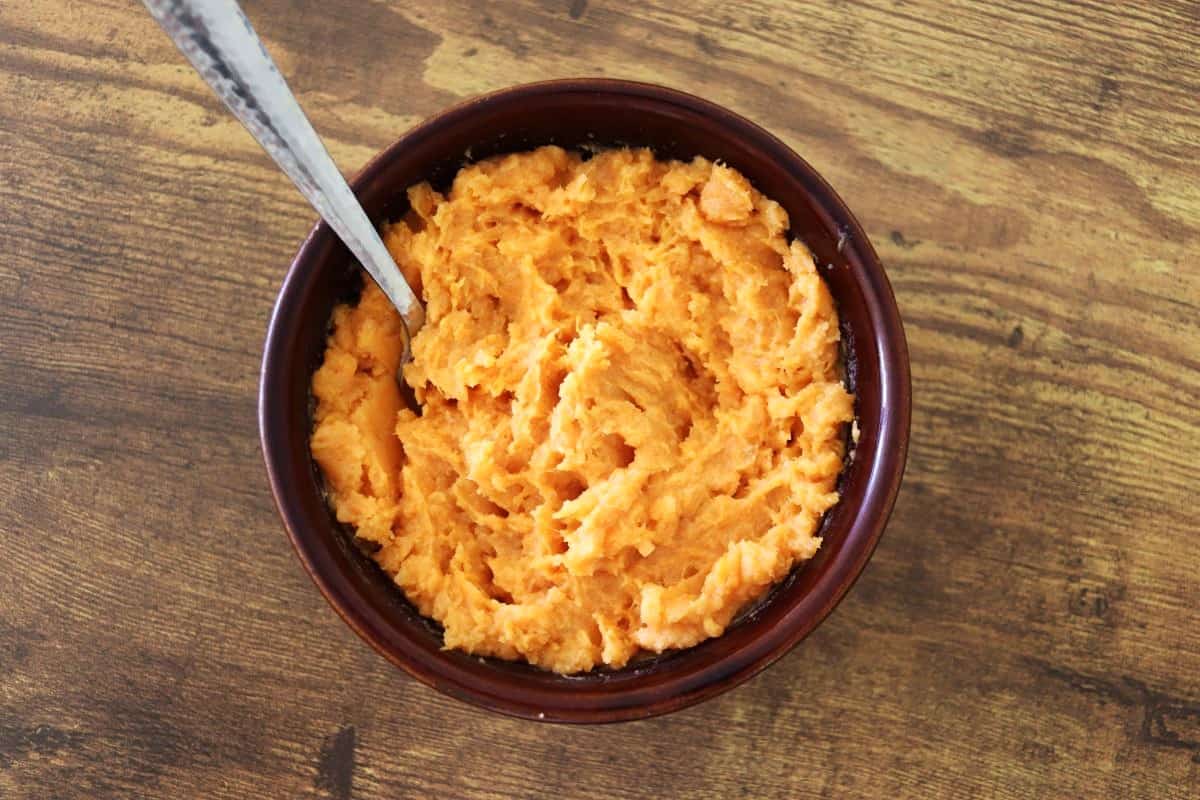 Mashed orange sweet potato mixture in a bowl with a fork in it.