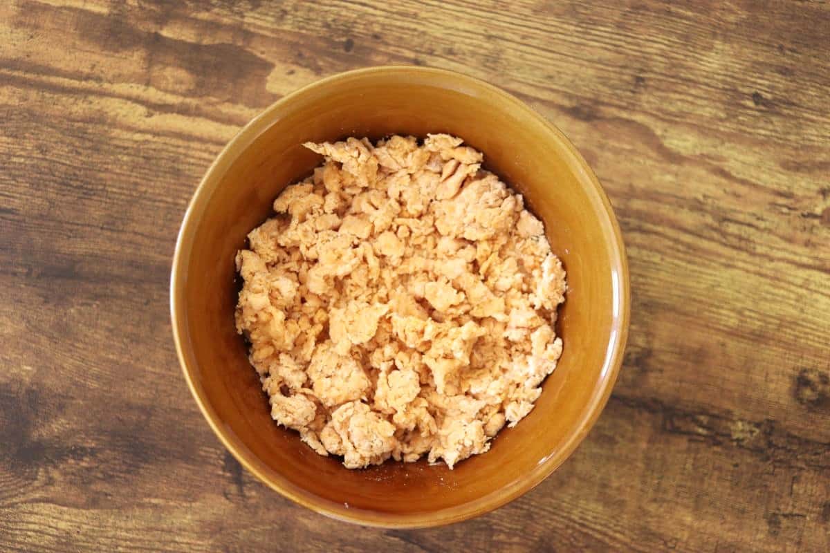 Shaggy, light orange dough in a bowl on a wooden surface.