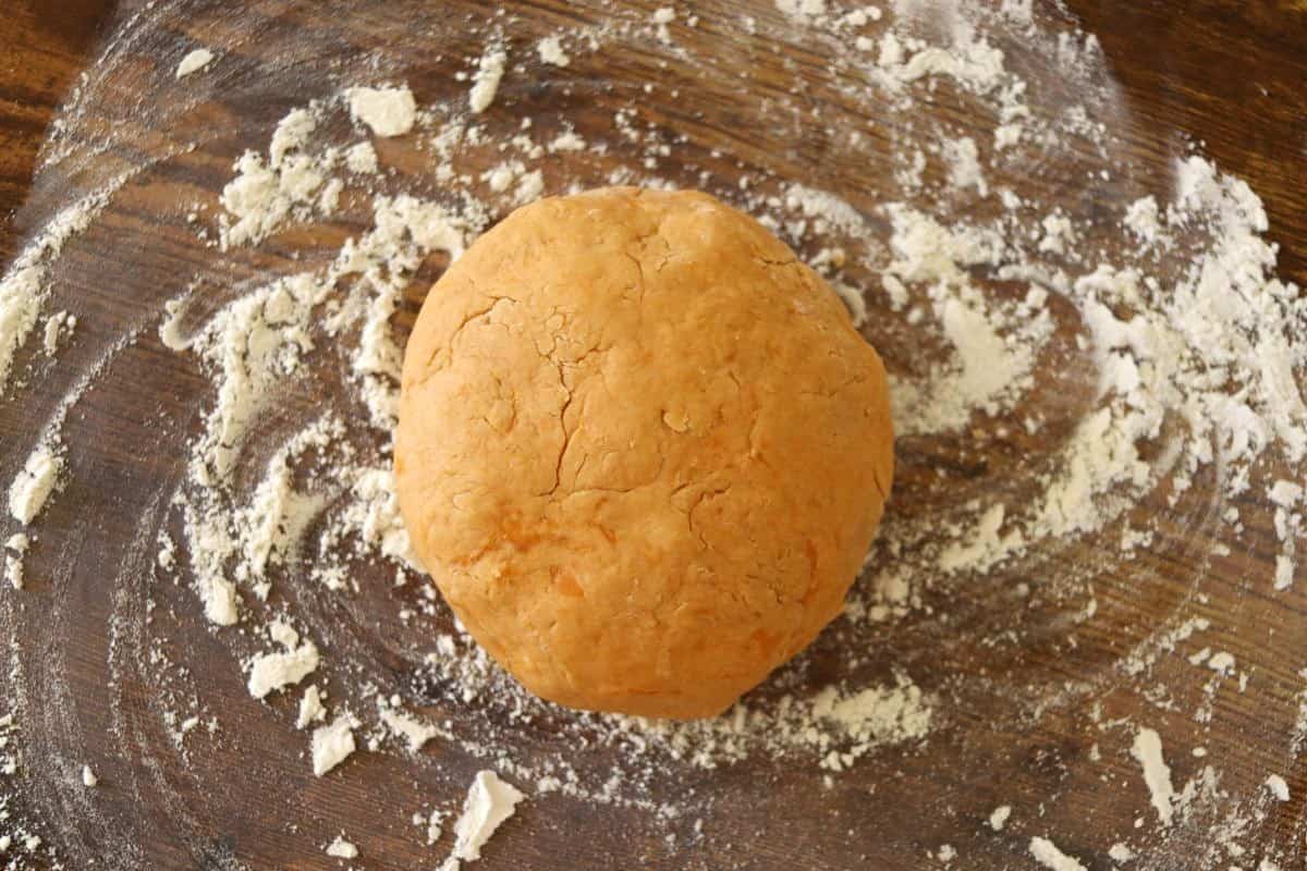 Orange dough ball sitting of a floured wooden surface.