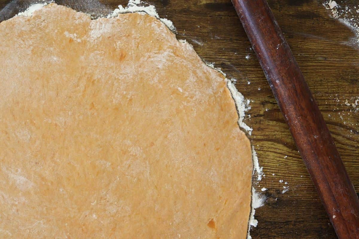 Orange dough rolled out on a wooden surface with flour along the edges.