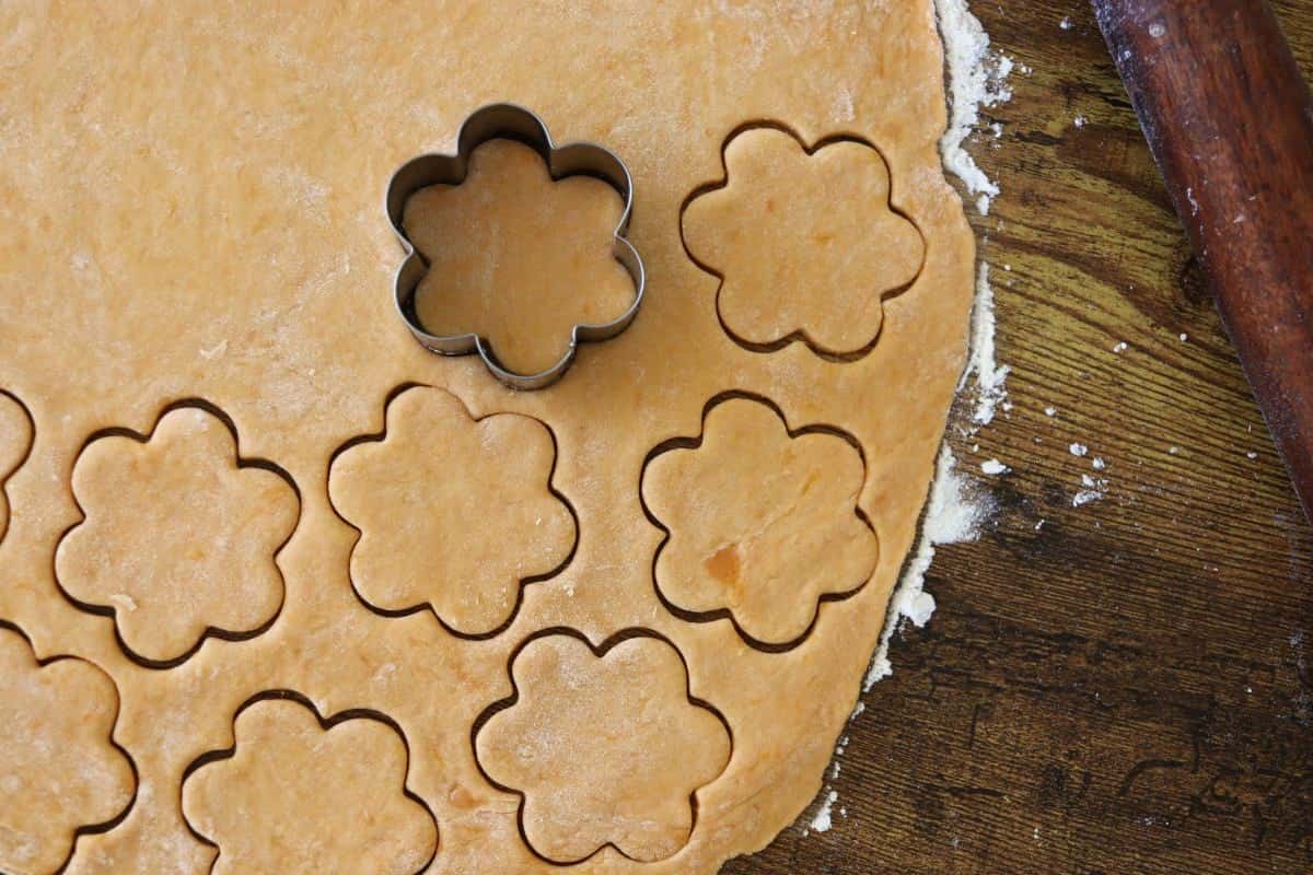 Flower shaped cutouts on rolled out orange dough with a cookie cutter sitting in one of the cutouts.