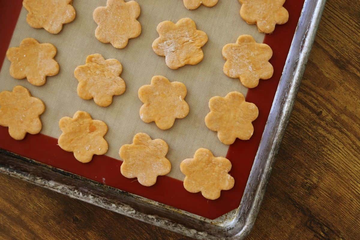 Flower shaped, orange crackers on a silicone lined baking sheet.
