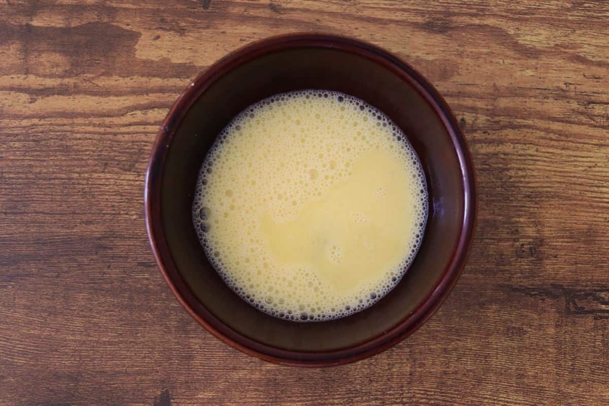 Beaten egg mixture in a brown bowl on a wooden surface.