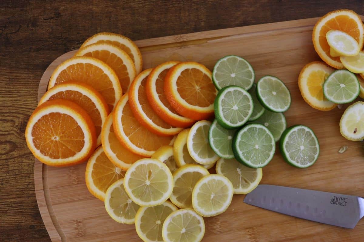 Slices of oranges, lemons, and limes on a wooden cutting board.