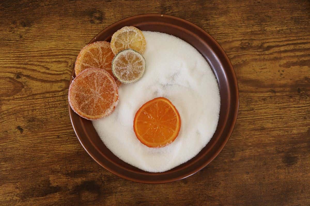 A brown plate full of sugar with a candied orange slice sitting in the center and several other citrus slices off to the side.