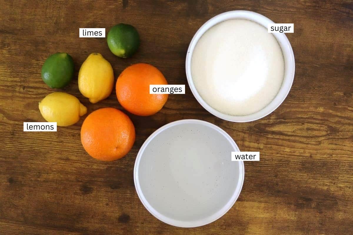 A wooden surface with two bowls, one filled with sugar and one with water. Beside them are two limes, two lemons, and two oranges, all labeled accordingly.
