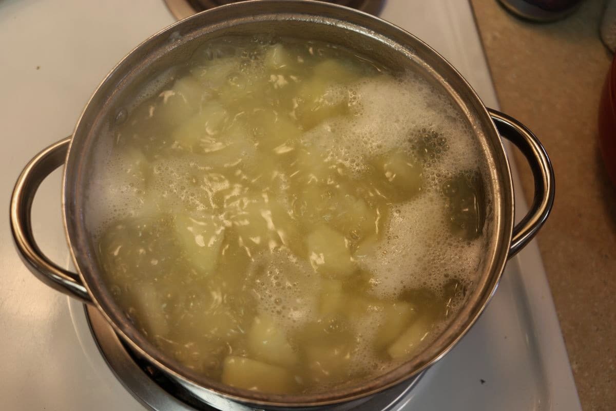 Cut up potatoes in a pot of simmering water on a stovetop.