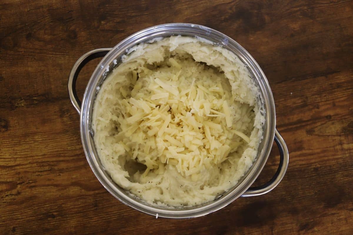 Mashed potatoes in a pot with shredded white cheddar cheese on top of them.