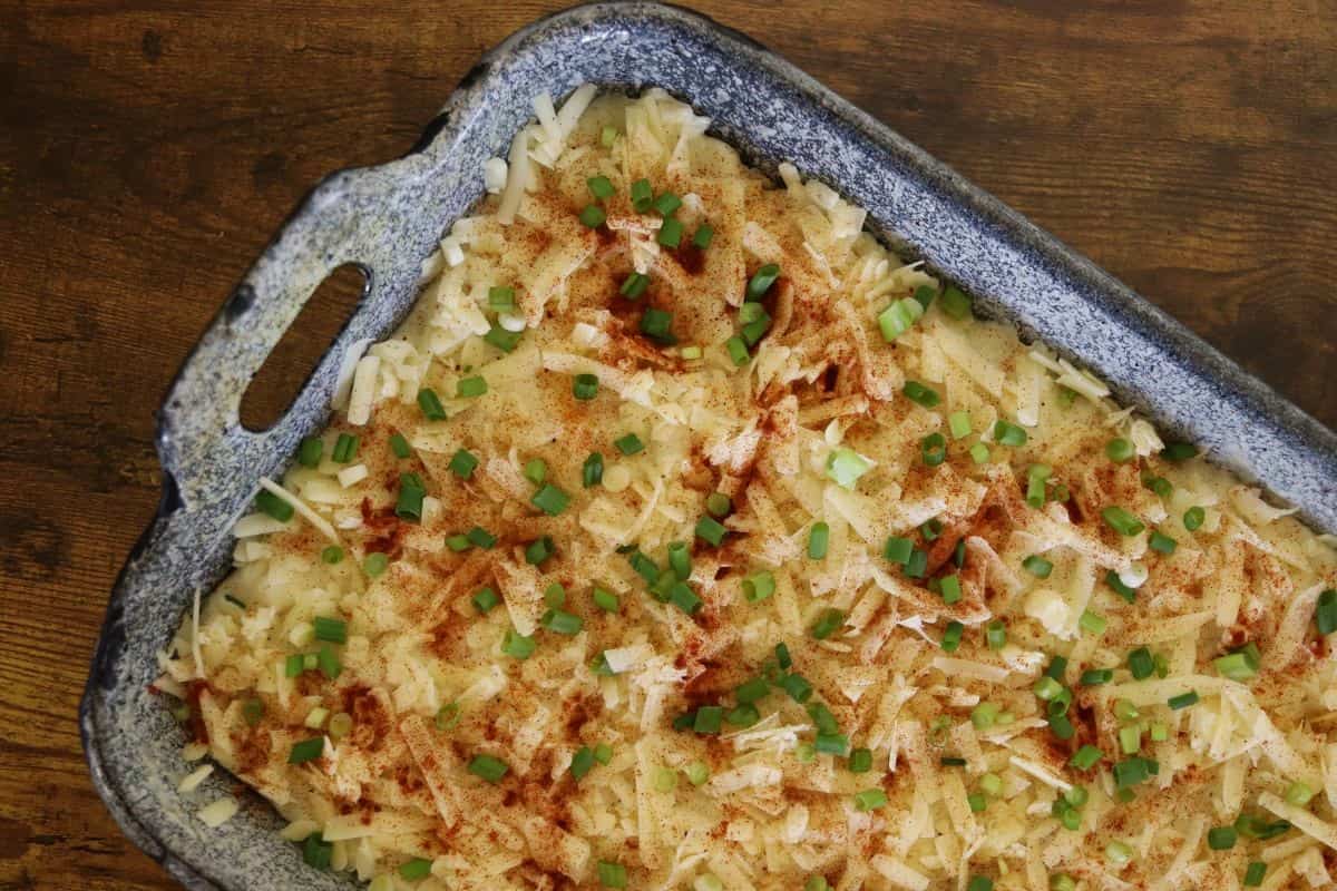 Mashed potatoes in a baking dish with shredded white cheese, paprika, and chopped scallions on top of them.