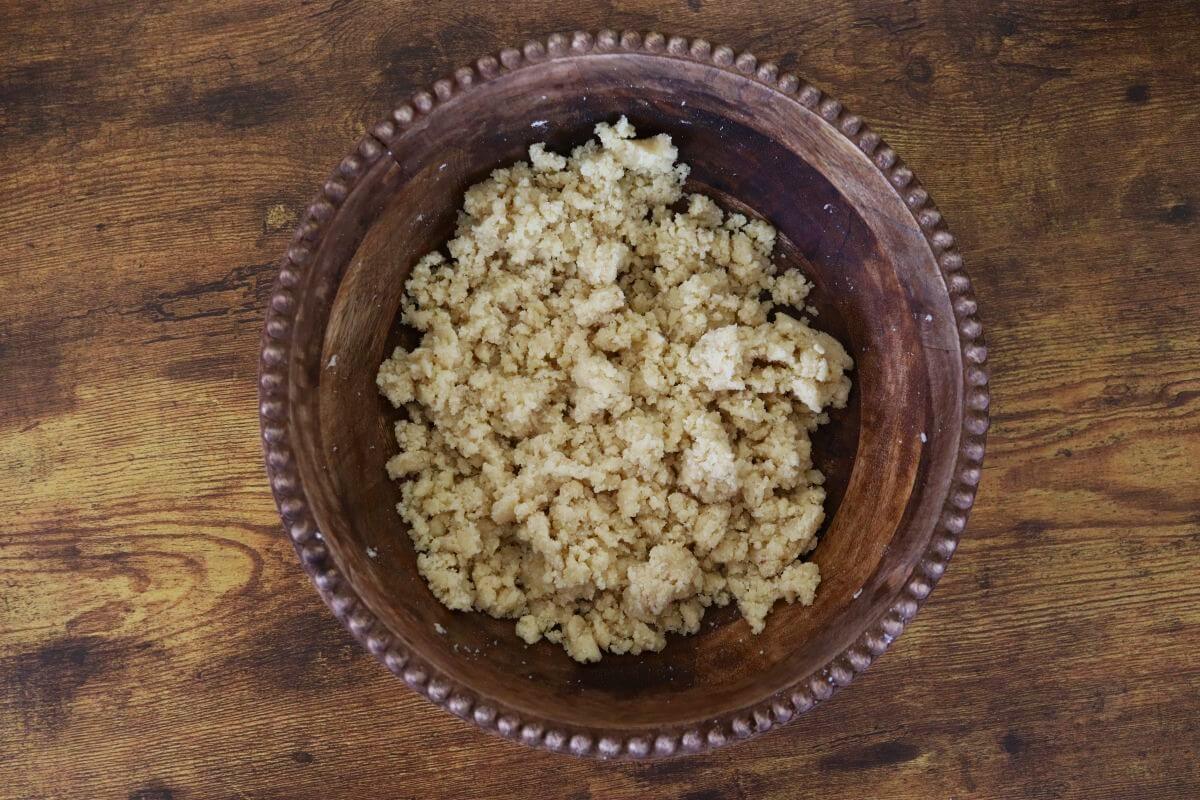 Crumbly, light tan dough mixture in a wooden bowl.