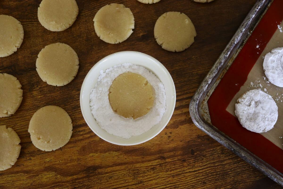 Round dough disk in a small condiment dish of white powder with other round dough disks next to it.