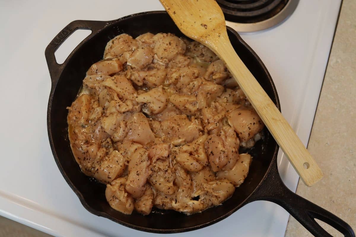 Raw turkey tips in a cast iron skillet, with a wooden spoon sitting on the edge of it, on a stovetop.
