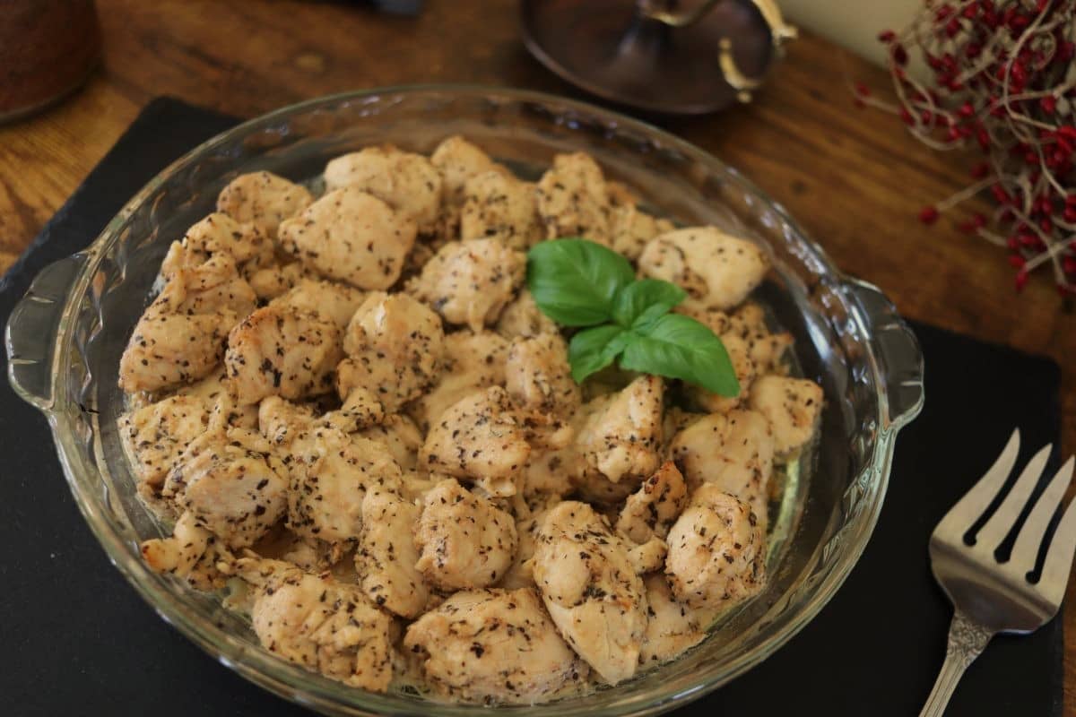 Cooked turkey tips, with seasoning on them and topped with fresh basil leaves, in a glass dish sitting on a slate board.