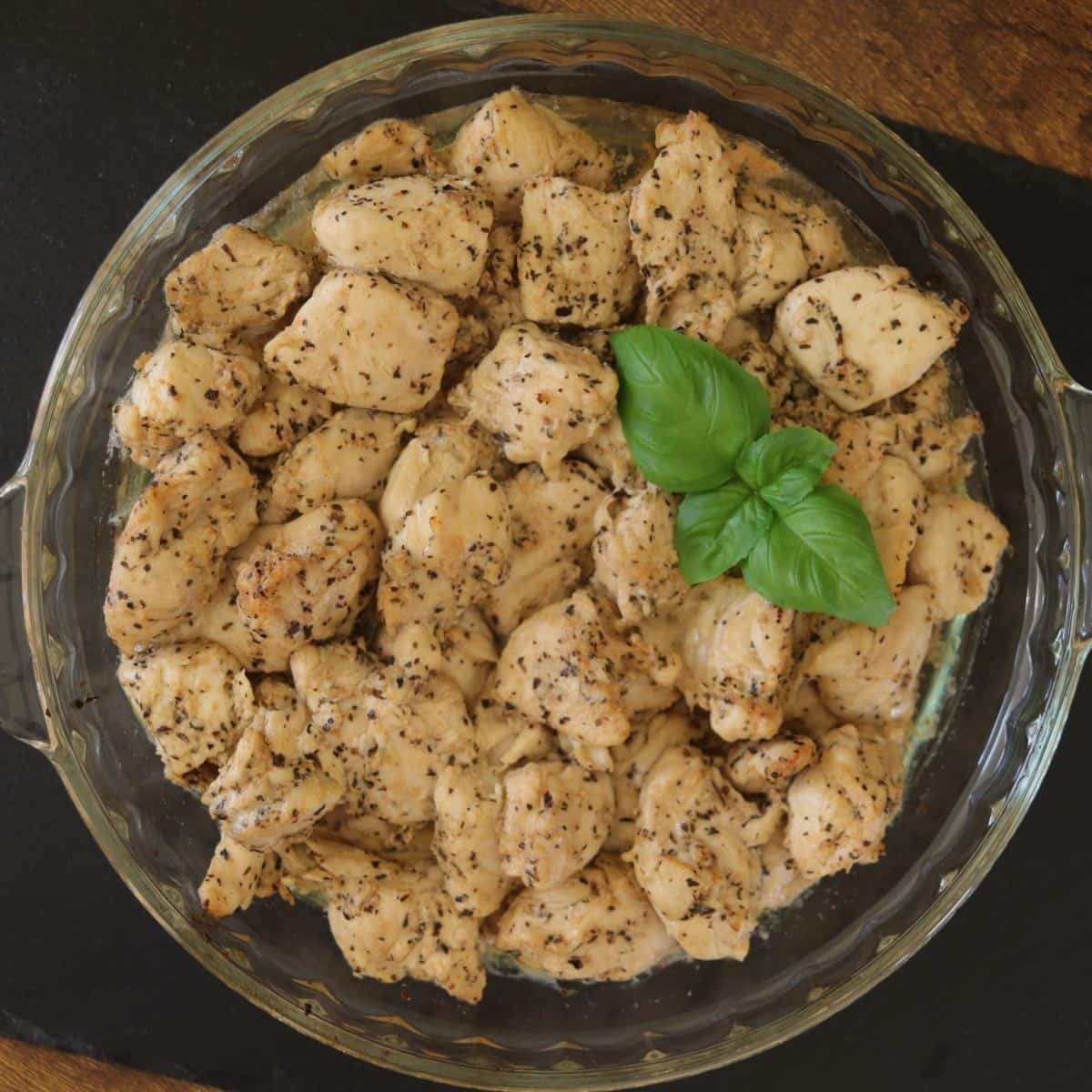 Cooked, seasoned turkey tips, with a sprig of fresh basil on top, in a round glass dish.