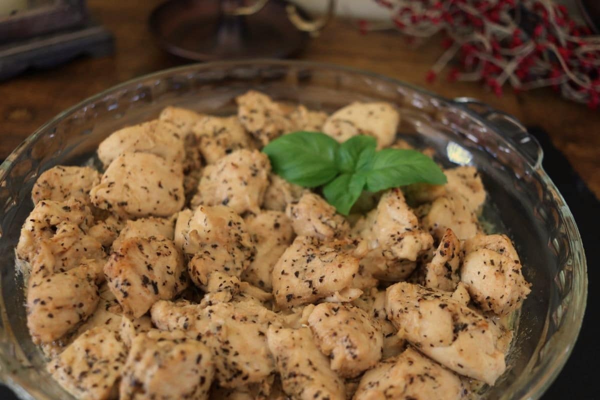 A glass dish filled with cooked, herb-seasoned turkey pieces, garnished with a sprig of fresh basil. Decorative red berries are in the background.