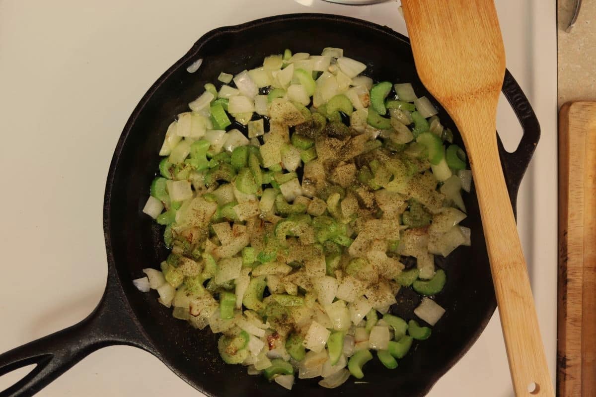 Celery and onions topped with ground sage in a cast iron skillet.