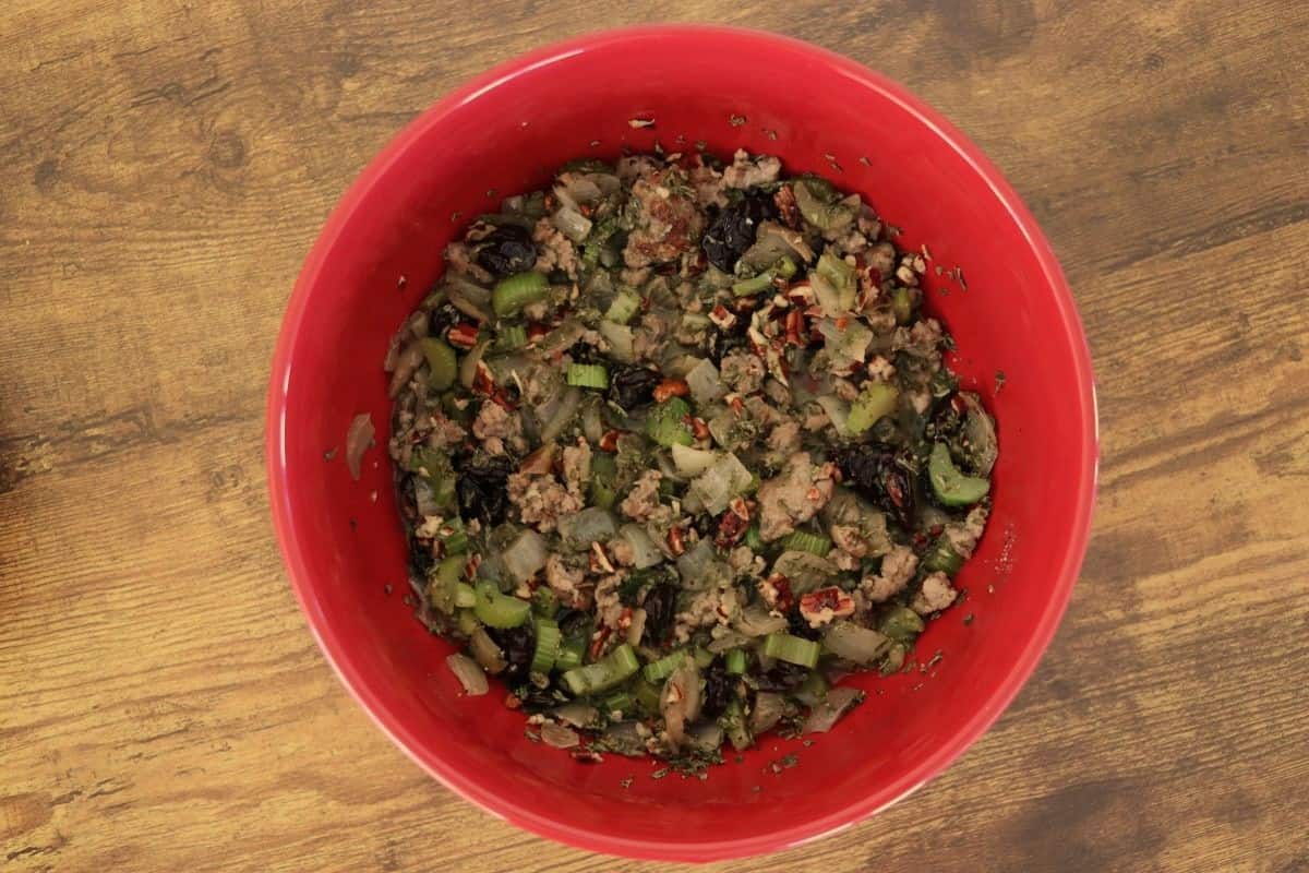 Celery, onion, sausage, pecans, cherries, and seasoning all mixed together in a red bowl.