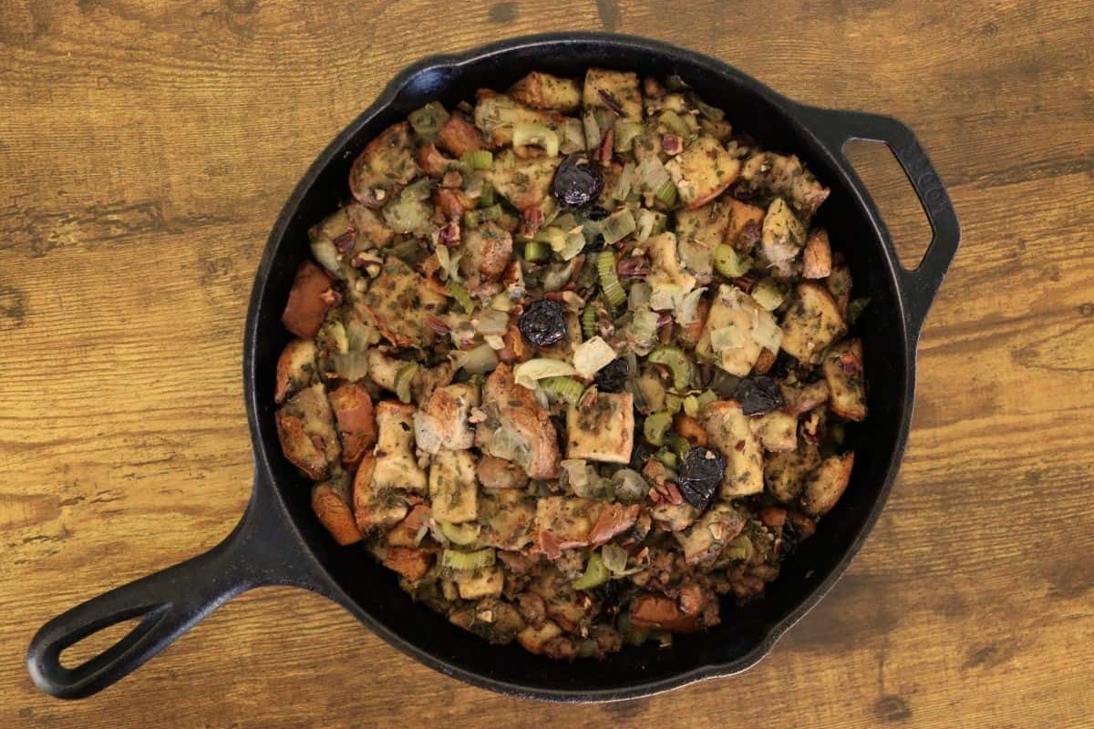Homemade stuffing, with celery, onions, pecans, sausage, cherries, and herbs in a cast iron skillet.