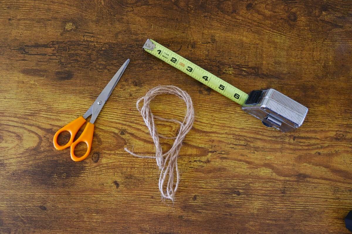 A tape measure, scissors, and length of jute twine on a wooden surface.
