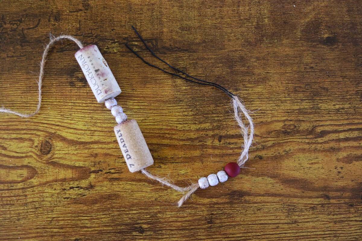 A wire folded in half with jute twine in the fold that has beads and wine corks strung on it.