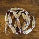 A garland made of wine corks, red beads, and white beads laying in a coil on a wooden surface.