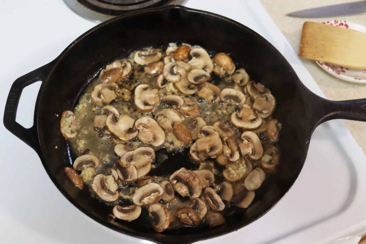 Sliced mushrooms sauteing with butter and garlic in a cast iron skillet.
