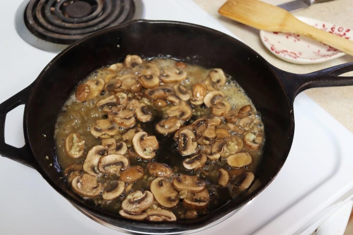 Sliced mushrooms cooking in a brandy and butter sauce in a cast iron skillet.