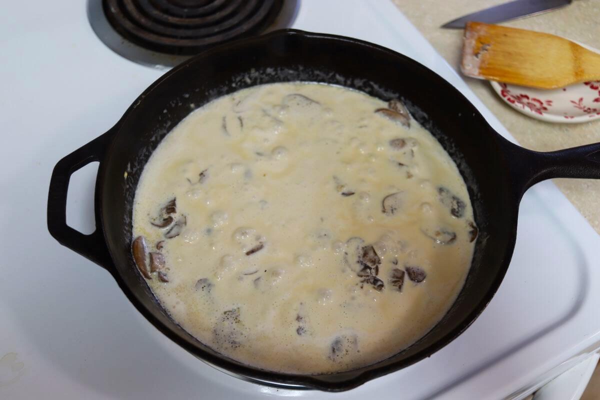 Creamy white sauce with mushrooms visible in it simmering in a cast iron skillet.
