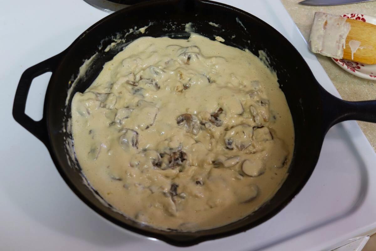 Thick white sauce with mushroom slices visible in it sitting the a stove in a cast iron skillet.