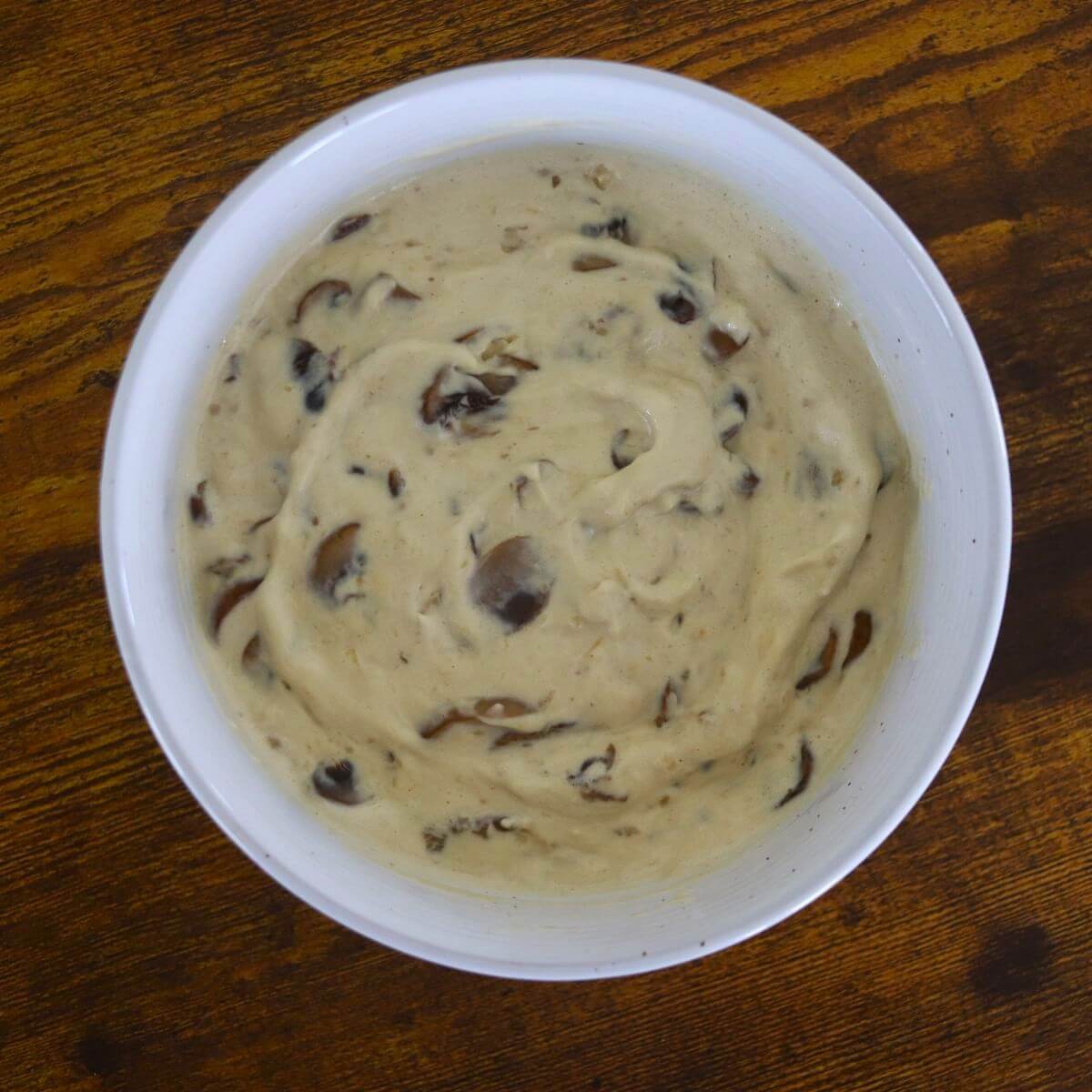 Creamy white sauce with mushrooms visible in it in a white bowl on a wooden surface.