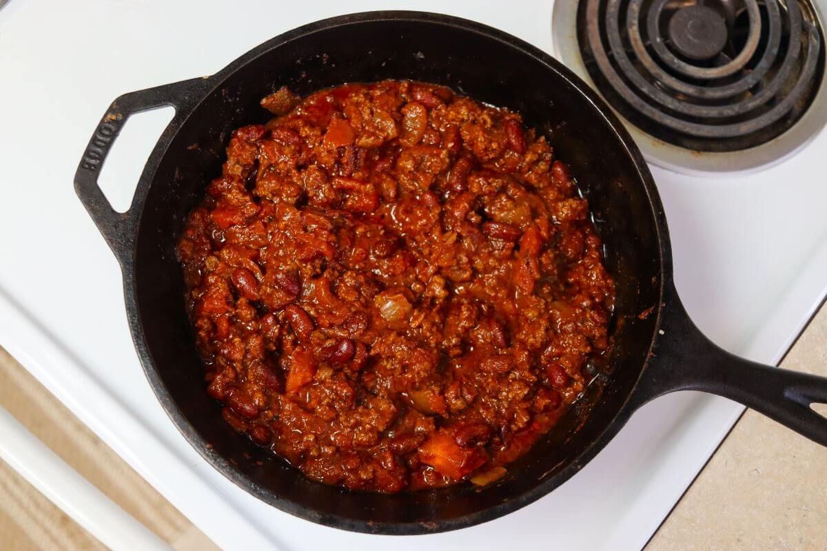 Cooked ground beef, kidney beans, and onions in a red sauce in a cast iron skillet.