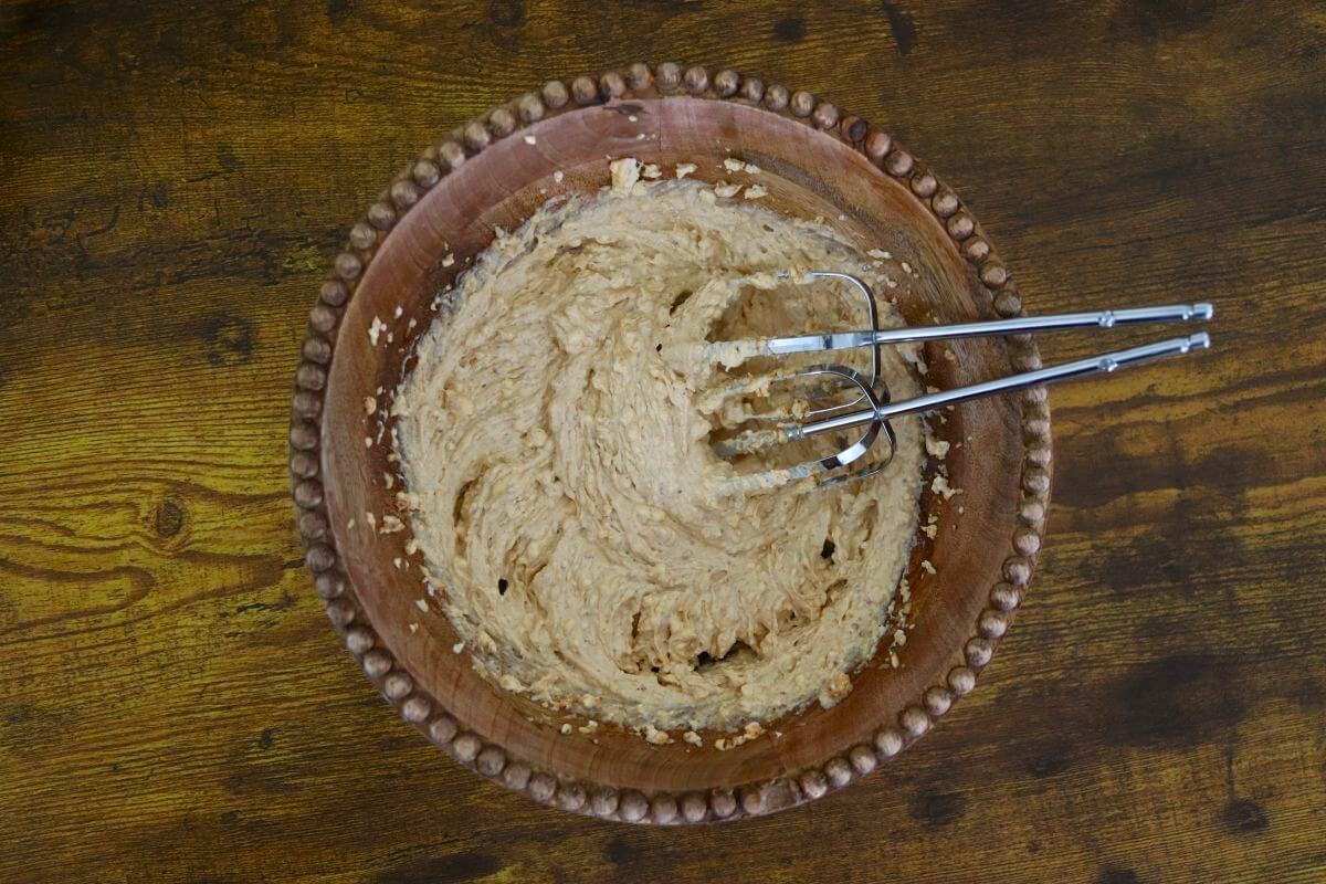 Creamy batter-like substance with a faint orange tint in a wooden bowl with two beater attachments in the bowl.