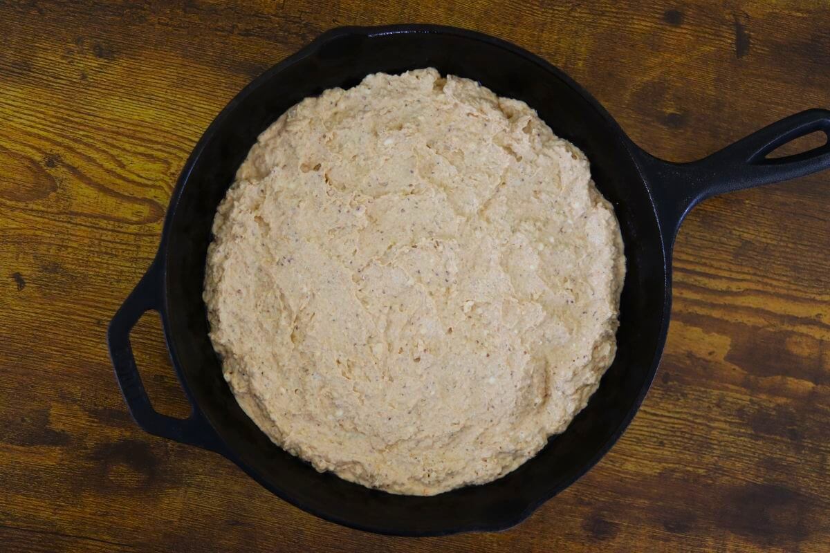 Creamy dip with a light orange tint spread over the bottom of a cast iron skillet.