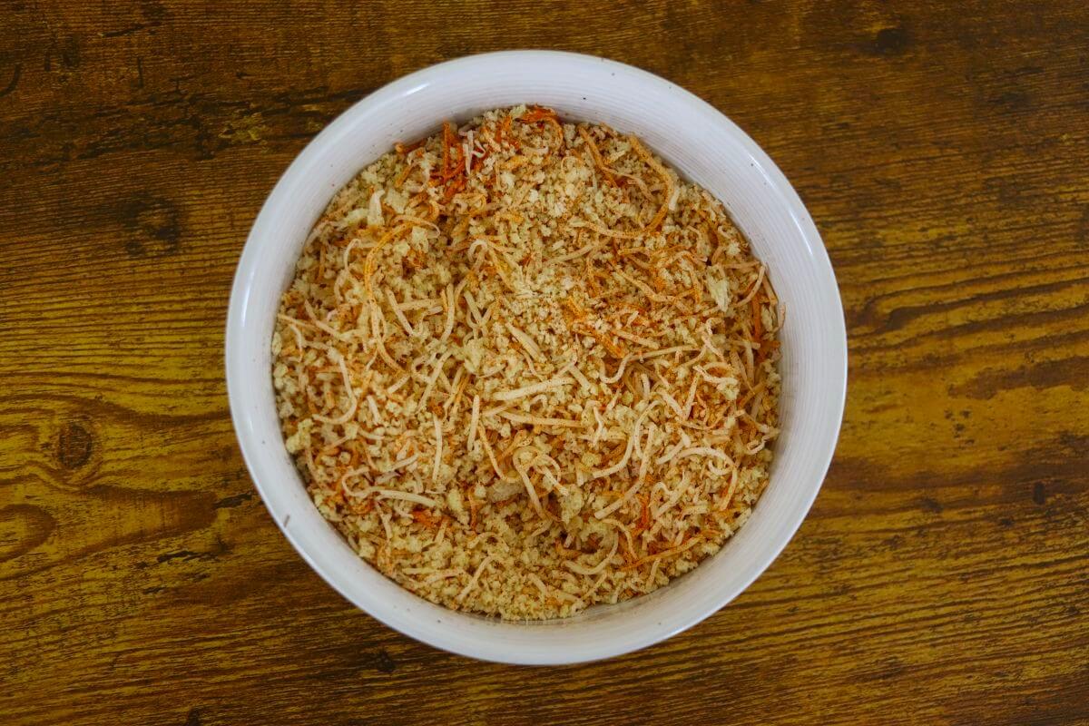 A mixture of bread crumbs, shredded cheese, and orange seasonings in a white bowl.