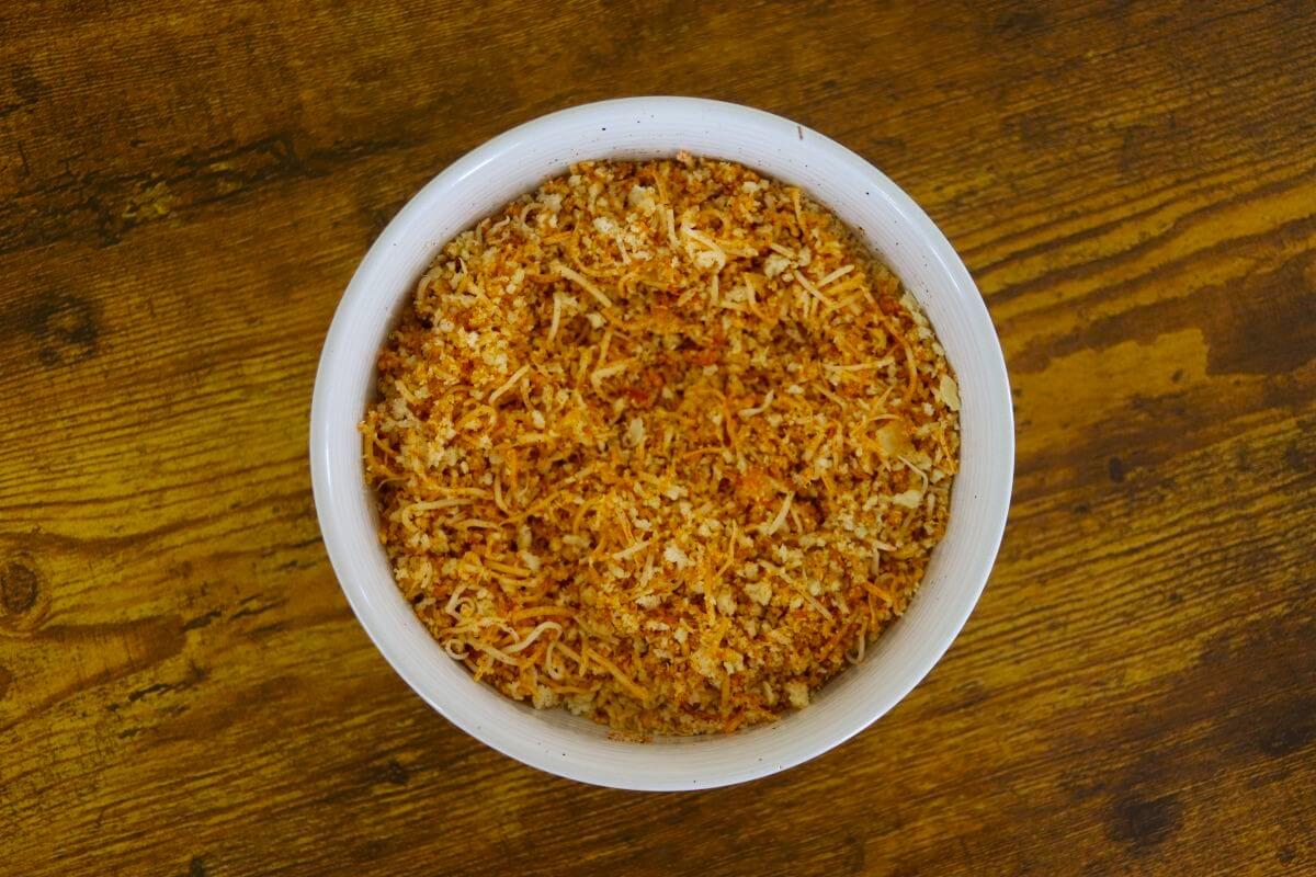 Shredded cheese, bread crumbs, and orange seasoning mixed together in a white bowl.