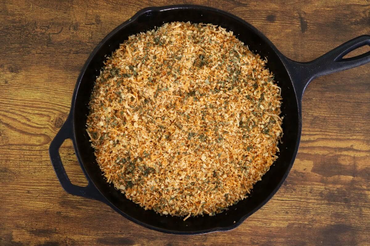 A cast iron skillet with a crumbly orange tinted mixture spread in it.